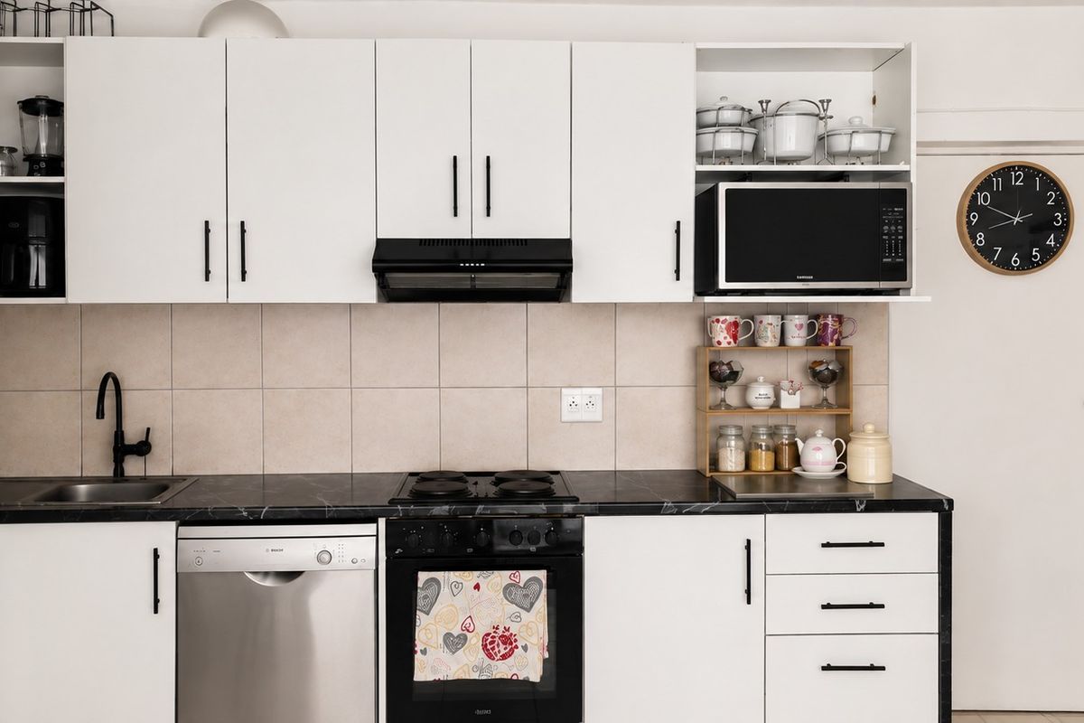A functional kitchen featuring white cabinetry, dark countertops, a tiled splashback, and integrated appliances including an oven, hob, and dishwasher.