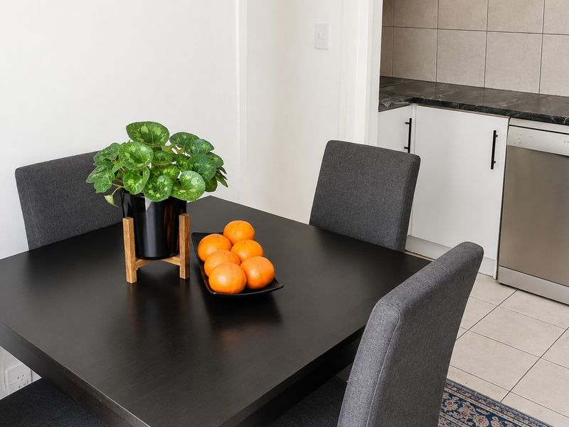 An open-plan dining area adjacent to a functional kitchen featuring tiled flooring, modern cabinetry, and built-in appliances.