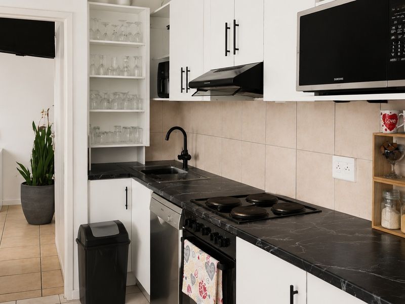 Compact modern kitchen featuring white cabinetry, black stone countertops, integrated appliances, and a tiled backsplash, offering efficient workspace and storage.