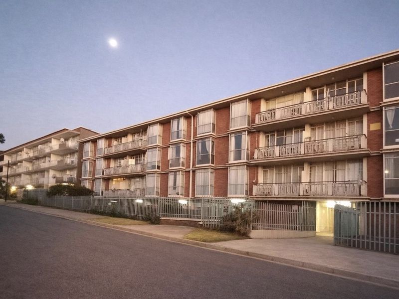 A multi-story commercial or residential apartment building featuring a brick facade, private balconies, and secure perimeter fencing along the street front.