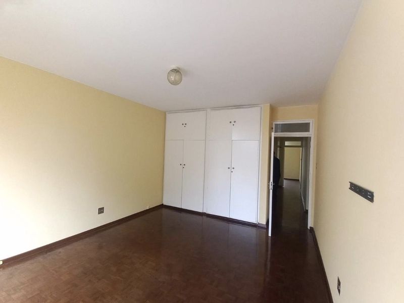 An empty bedroom featuring parquet flooring, built-in cupboards, and neutral wall paint, offering a blank canvas for potential occupants.