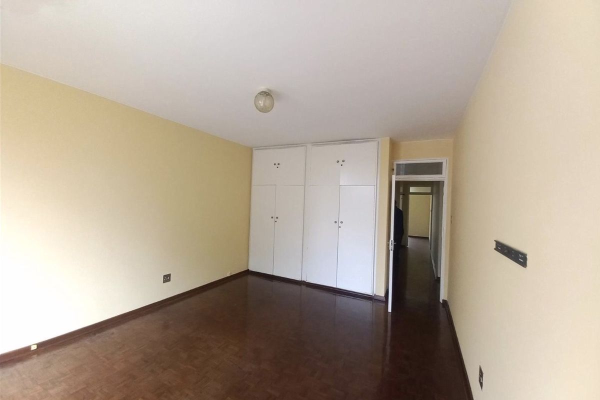 An empty bedroom featuring parquet flooring, built-in cupboards, and neutral wall paint, offering a blank canvas for potential occupants.