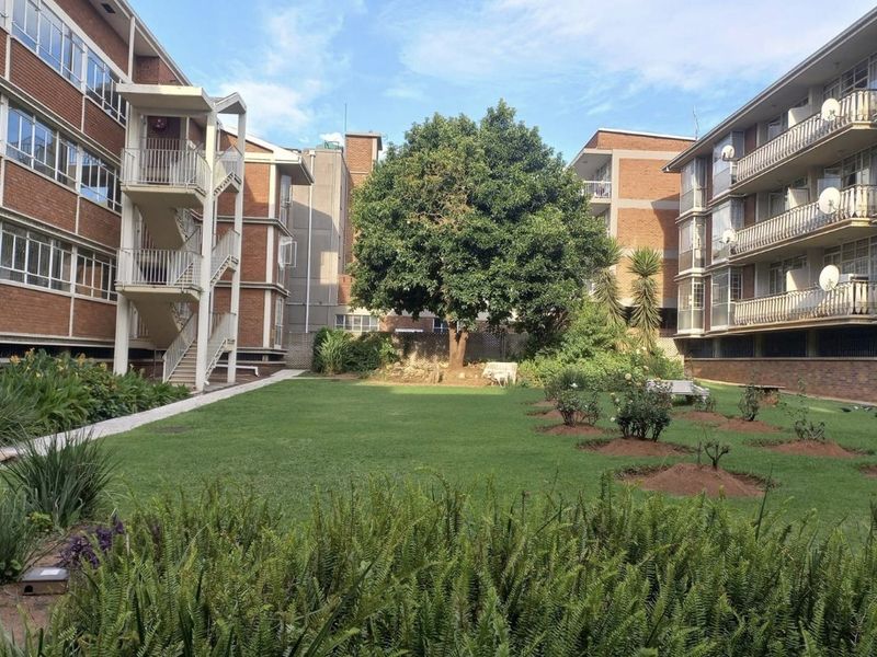 A well-maintained communal garden area situated between two multi-story brick commercial or residential buildings, featuring paved walkways and external staircases.