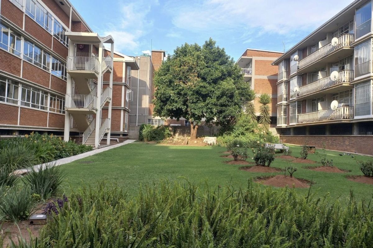 A well-maintained communal garden area situated between two multi-story brick commercial or residential buildings, featuring paved walkways and external staircases.