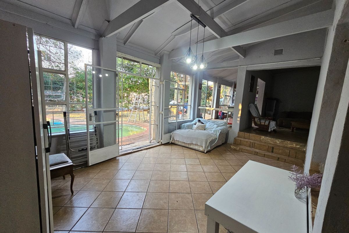 Spacious living area featuring vaulted ceilings with exposed beams, tiled flooring, and large glass doors providing direct access to the pool area.