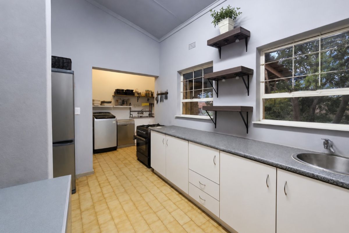 Functional kitchen featuring white cabinetry, laminate countertops, a stainless steel sink, and a connected scullery area with laundry facilities.