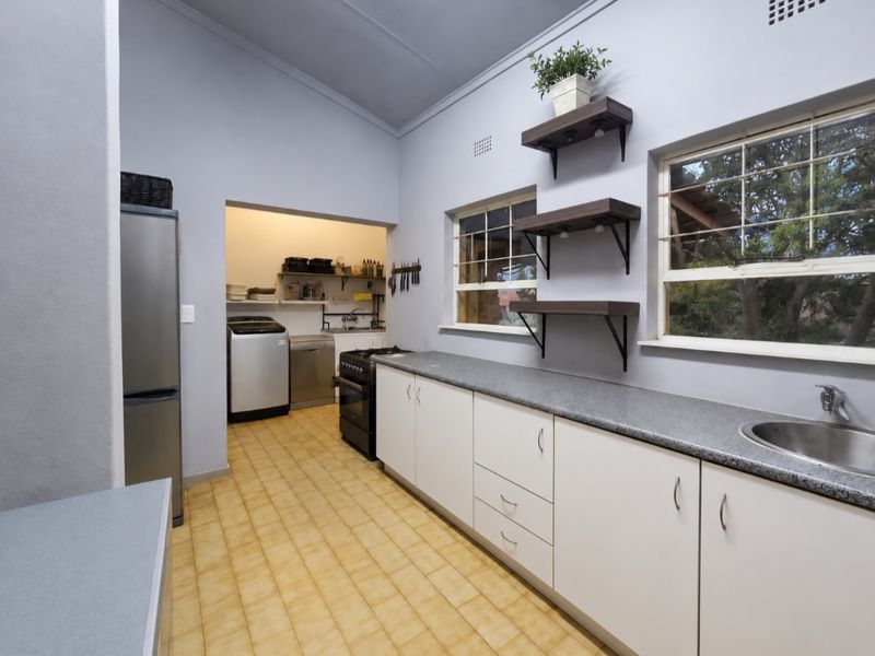 Functional kitchen featuring white cabinetry, laminate countertops, a stainless steel sink, and a connected scullery area with laundry facilities.
