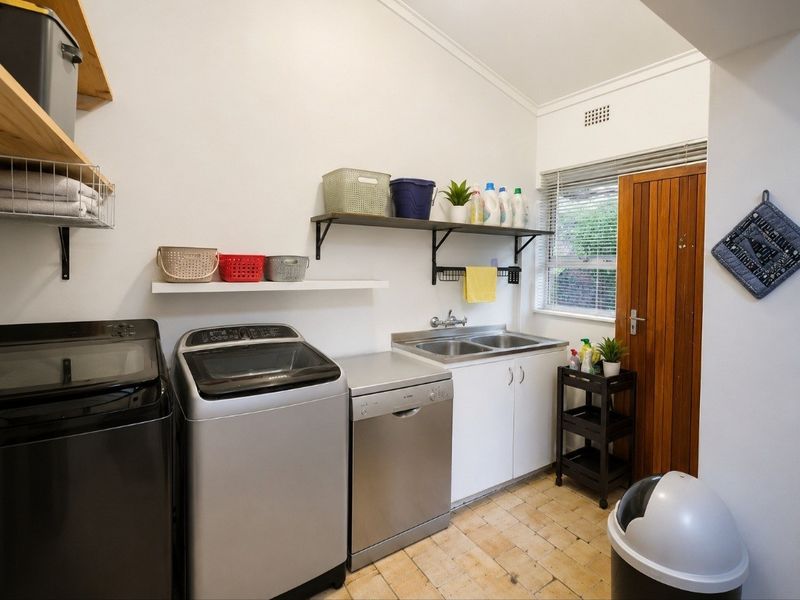 Functional laundry room featuring a double stainless steel sink, built-in cabinetry, wall-mounted shelving, and tiled flooring with direct access to the exterior.