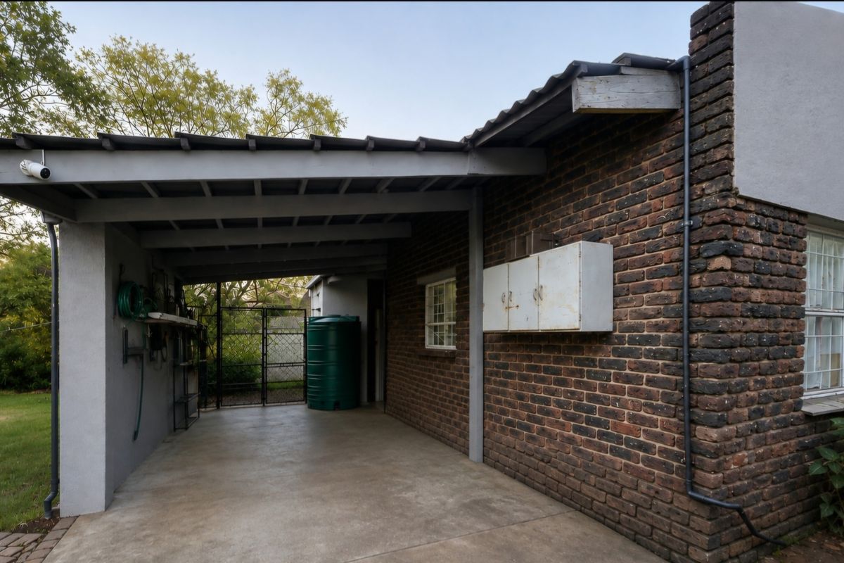 A covered rear patio area featuring exposed brick walls, concrete flooring, a water storage tank, and secure gated access to the garden.