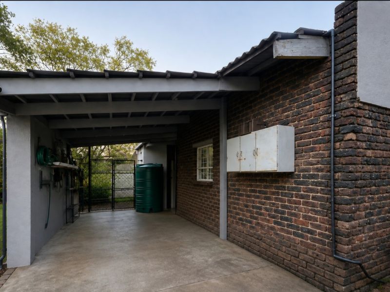 A covered rear patio area featuring exposed brick walls, concrete flooring, a water storage tank, and secure gated access to the garden.