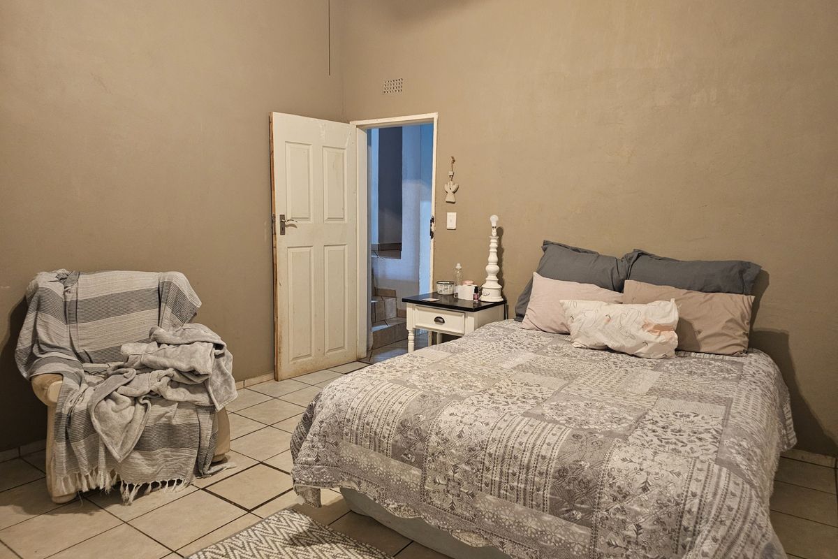 A bedroom featuring tiled flooring and neutral wall tones, providing a functional space with direct access to an adjacent hallway.