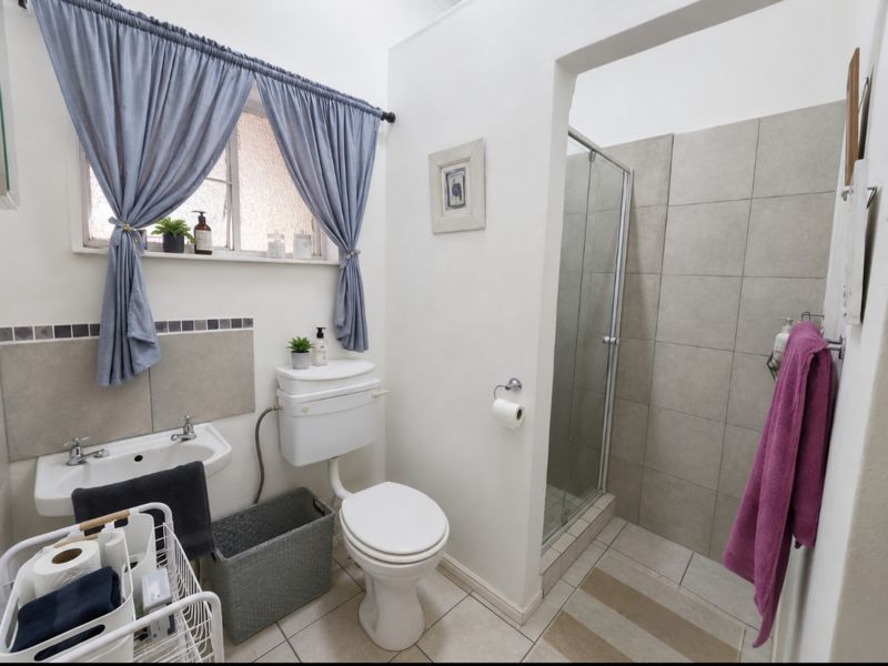 A functional bathroom featuring a walk-in shower with tiled surround, pedestal basin, and toilet, finished with neutral ceramic floor tiles.