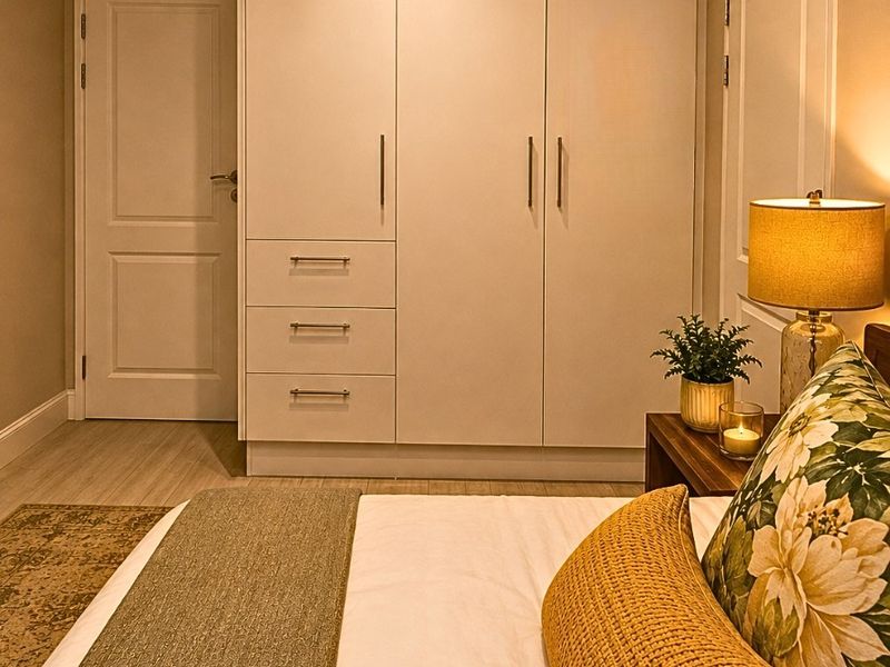 A well-maintained bedroom featuring built-in wardrobes with integrated drawers, neutral wall finishes, and light-toned laminate flooring.