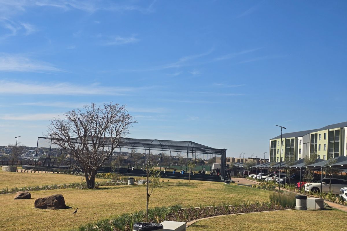 A well-maintained communal garden area featuring landscaped lawns, paved pathways, and access to on-site sports facilities and covered parking bays.