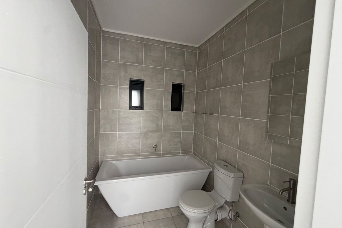 Modern bathroom featuring a freestanding bathtub, pedestal basin, and neutral grey wall and floor tiling.