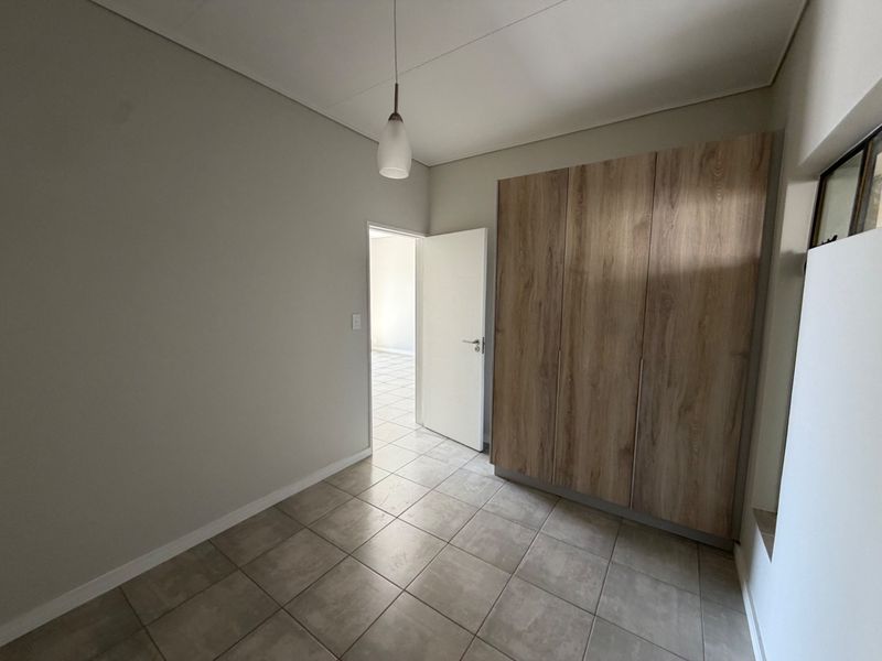 A clean, empty bedroom featuring neutral tiled flooring and modern wood-finish built-in cupboards, offering a versatile space ready for personalization.