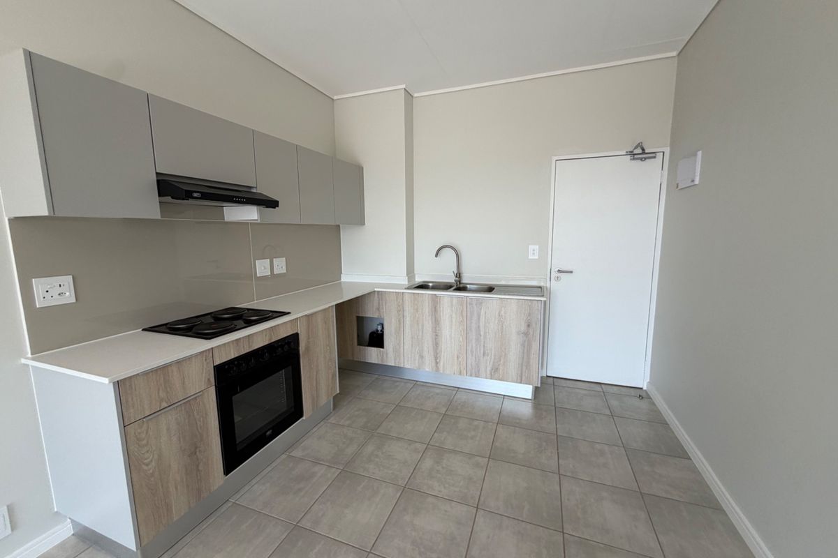 Modern kitchen featuring light wood-grain cabinetry, stone countertops, integrated electric hob and oven, and neutral tiled flooring in a clean, contemporary space.