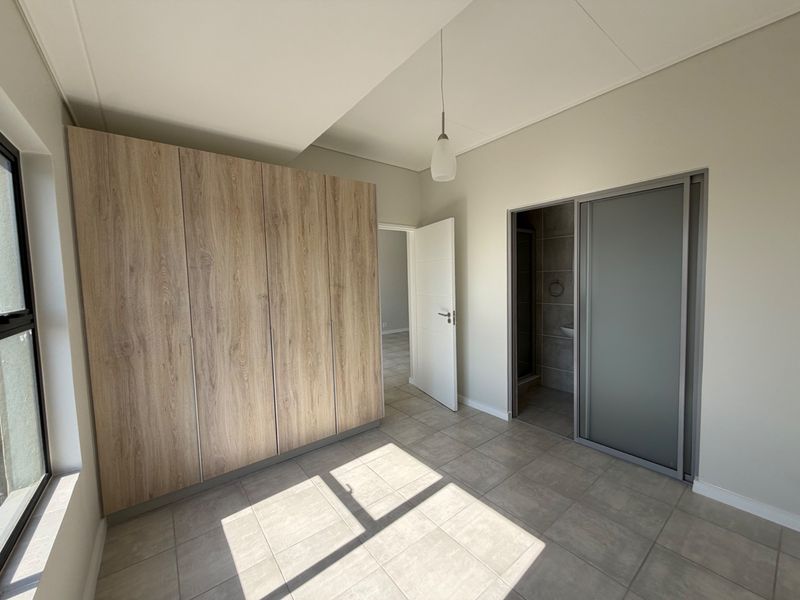 A bright, modern bedroom featuring neutral tiled flooring, ample built-in wooden cupboards, and direct access to an en-suite bathroom.