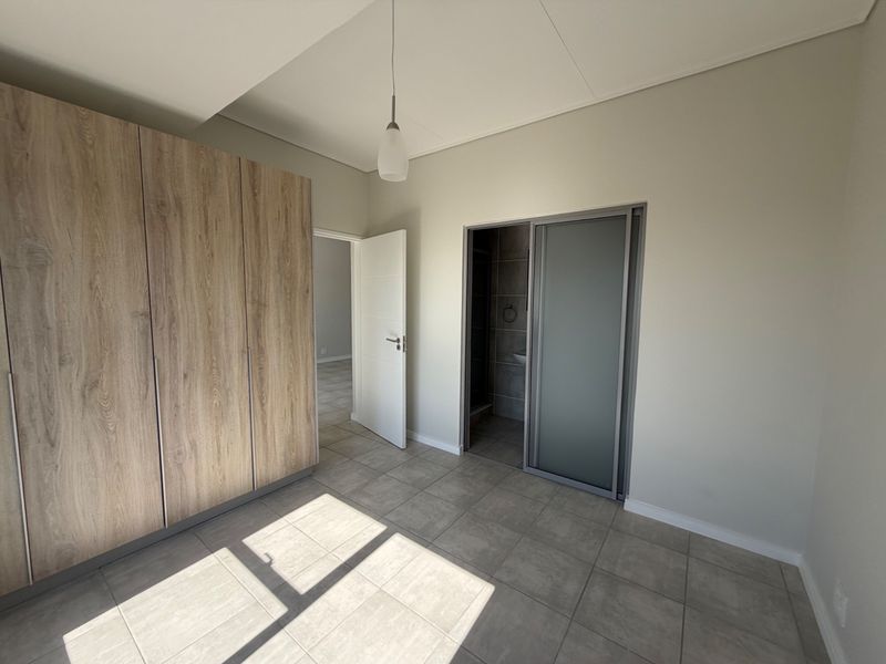 A bright, empty bedroom featuring modern wood-finish built-in cupboards, neutral tiled flooring, and direct access to an en-suite bathroom.