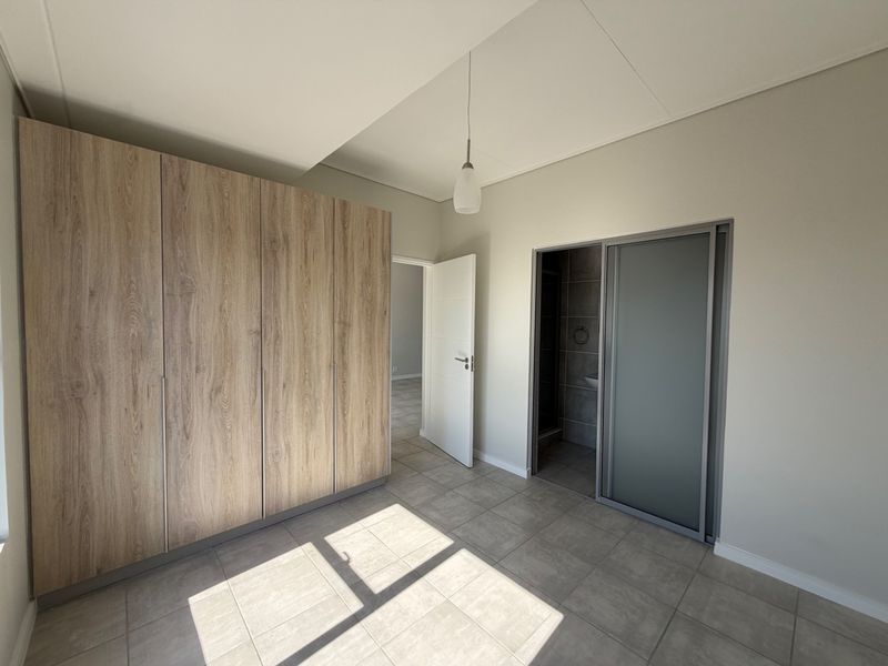 A bright, empty bedroom featuring modern wood-finish built-in wardrobes, tiled flooring, and an en-suite bathroom access point.