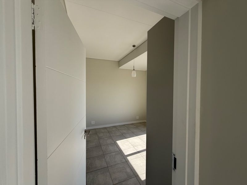 A bright, empty bedroom featuring neutral wall tones, tiled flooring, and a modern pendant light fixture, ready for personalization.