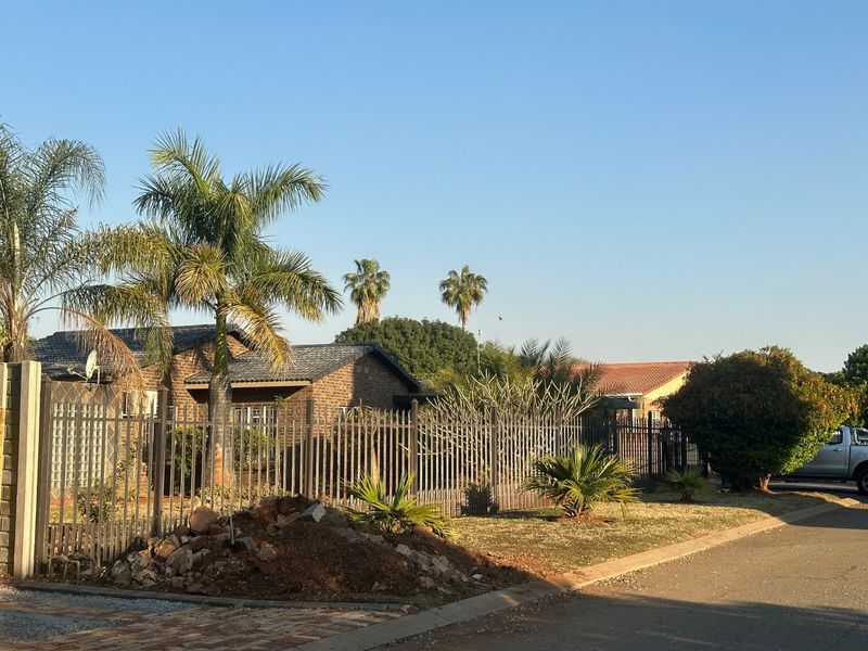 Front exterior view of a brick house featuring a tiled roof, metal perimeter fencing, and a paved driveway with some landscaping debris on the verge.