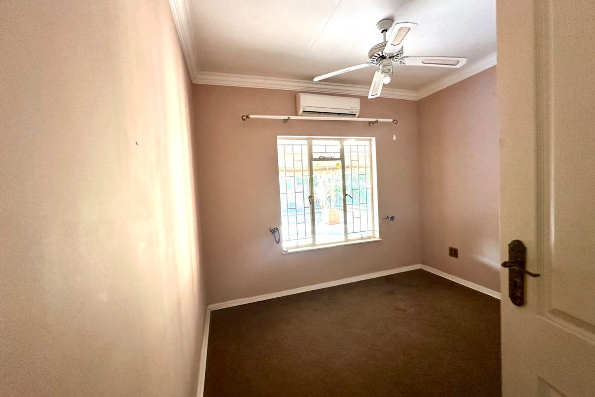 An empty bedroom featuring a ceiling fan, split-system air conditioning, and security bars on the window.