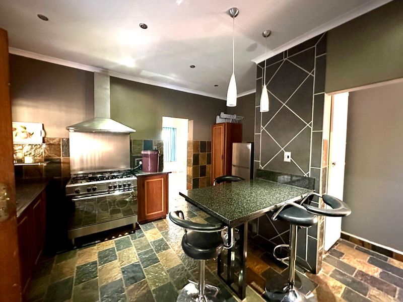 A functional kitchen featuring a gas stove, stainless steel extractor, granite breakfast bar, and distinctive slate tile flooring with a decorative tiled feature wall.