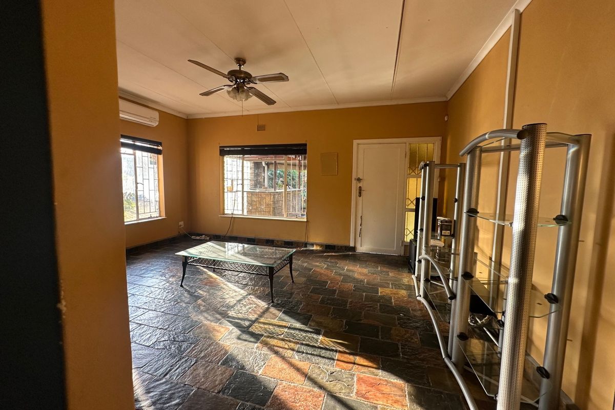 Spacious living area featuring durable slate tile flooring, a ceiling fan, and a wall-mounted air conditioning unit.