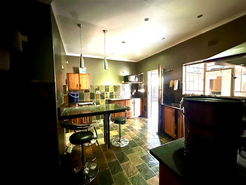 A functional kitchen featuring stone tile flooring, stone countertops, built-in wooden cabinetry, and a breakfast bar area with pendant lighting.