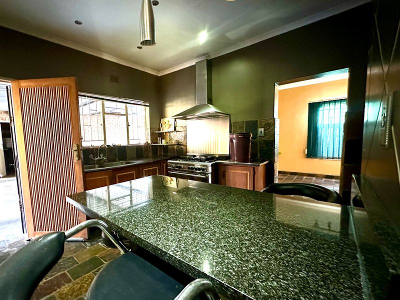 A functional kitchen featuring granite countertops, a stainless steel extractor fan, gas stove, and stone tile flooring with direct access to adjacent living spaces.