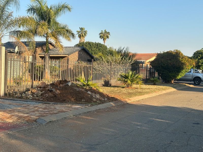 Street view of a residential property featuring a brick facade, tiled roof, and metal security fencing with a paved driveway entrance.