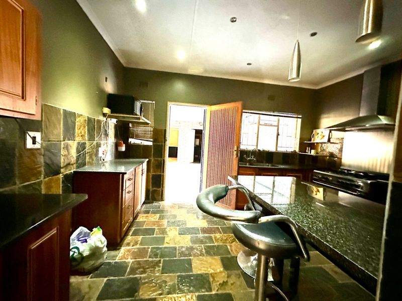 A functional kitchen featuring granite countertops, wooden cabinetry, stone tile flooring, and a built-in gas hob with a stainless steel extractor fan.