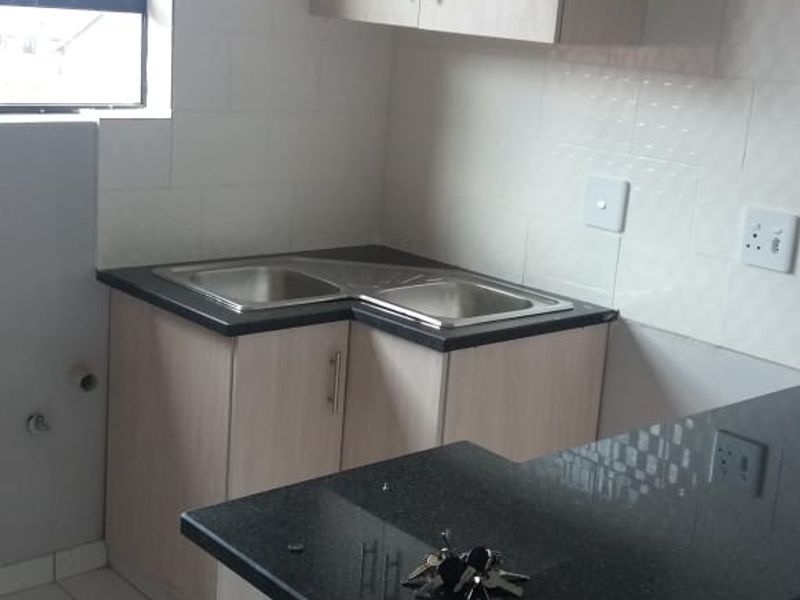 A compact, functional kitchen featuring light wood-finish cabinetry, dark granite countertops, a double sink, and a breakfast nook with tiled flooring.