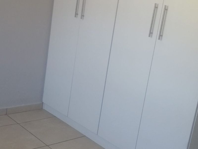 A clean, empty bedroom featuring neutral tiled flooring and modern white built-in cupboards with sleek metal handles.
