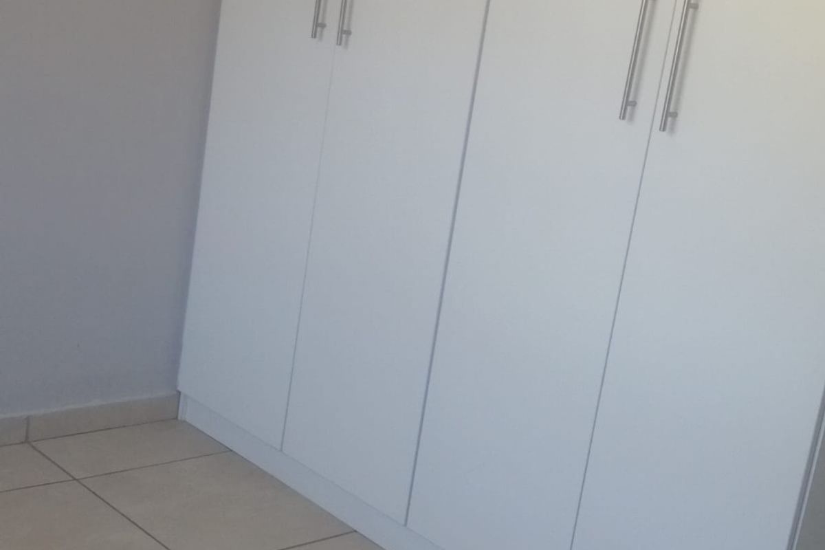 A clean, empty bedroom featuring neutral tiled flooring and modern white built-in cupboards with sleek metal handles.