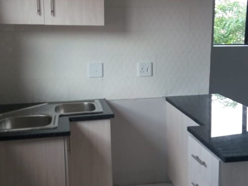 A functional kitchen featuring light wood-tone cabinetry, dark granite countertops, a double sink, and neutral tiled flooring, offering a clean, blank canvas for customization.