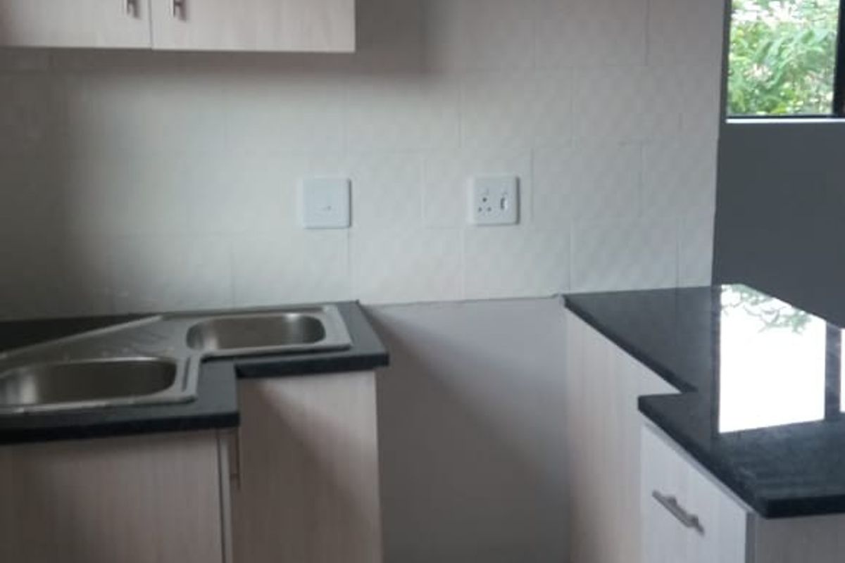 A functional kitchen featuring light wood-tone cabinetry, dark granite countertops, a double sink, and neutral tiled flooring, offering a clean, blank canvas for customization.