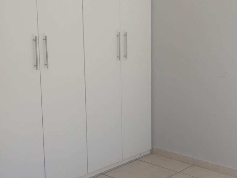 A clean, empty bedroom featuring neutral tiled flooring and modern white built-in cupboards.