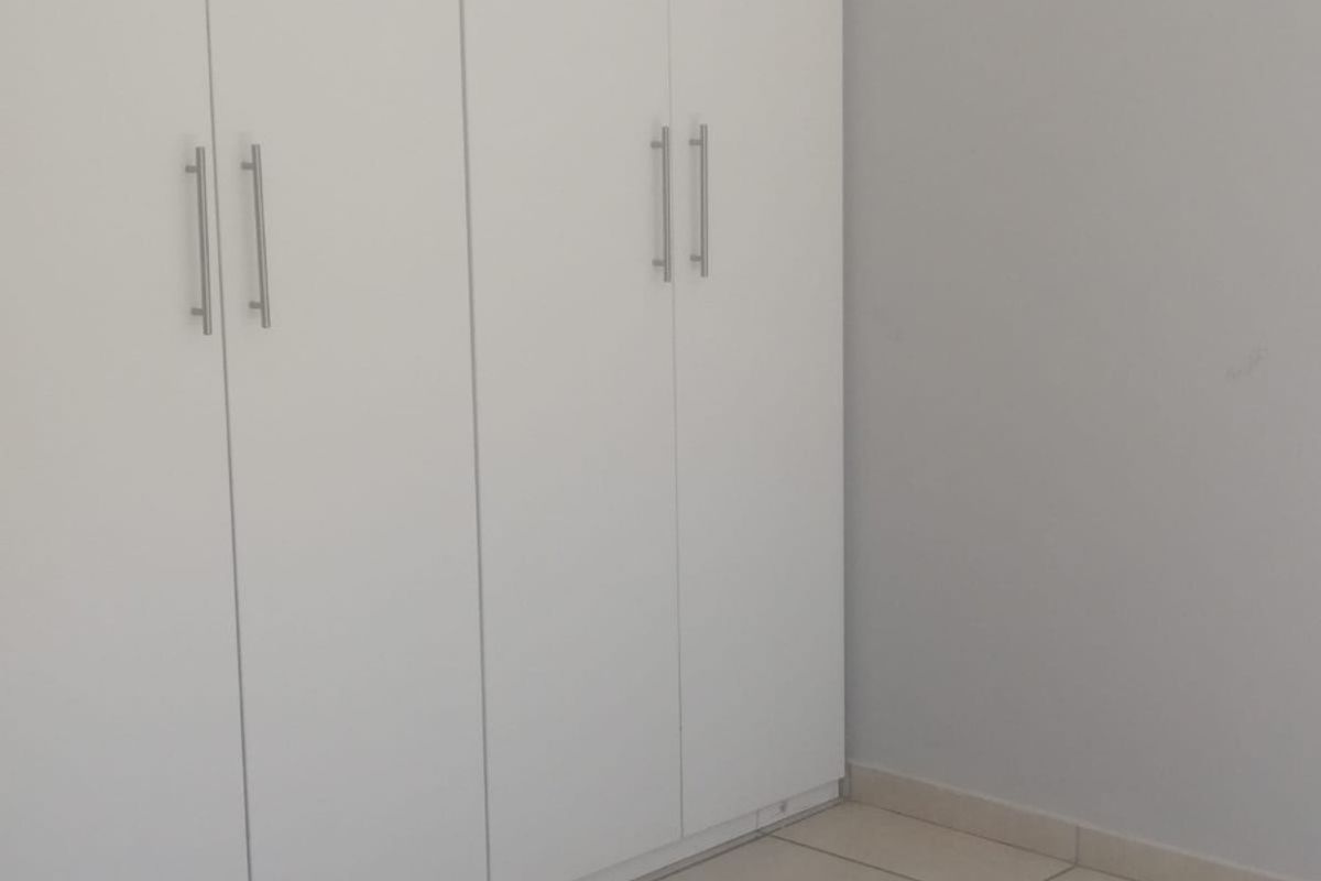 A clean, empty bedroom featuring neutral tiled flooring and modern white built-in cupboards.