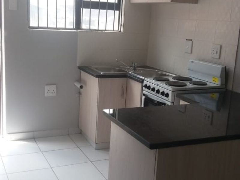 A compact kitchen featuring light wood-finish cabinetry, granite countertops, tiled flooring, and a built-in electric stove with security bars on the window.