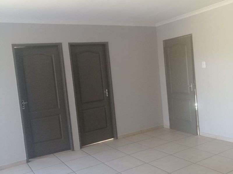 A clean, empty hallway featuring neutral wall paint, light-colored floor tiles, and three dark-toned interior doors.