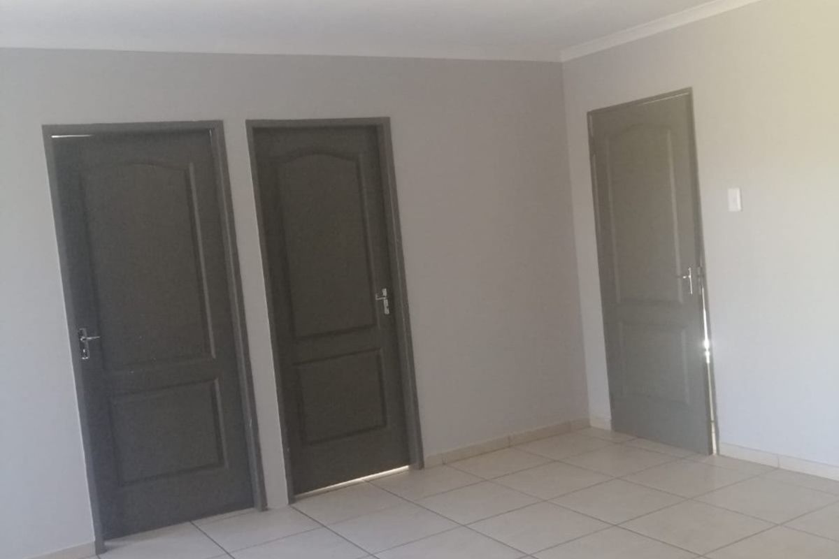 A clean, empty hallway featuring neutral wall paint, light-colored floor tiles, and three dark-toned interior doors.