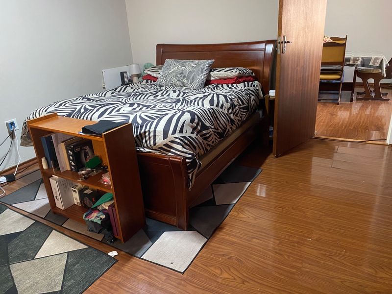 A bedroom featuring laminate flooring and a timber door, with a view into an adjacent dining area.