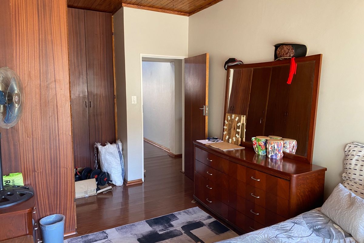 A bedroom featuring built-in wooden cupboards, a wooden ceiling, and laminate flooring, offering a dated but functional living space.