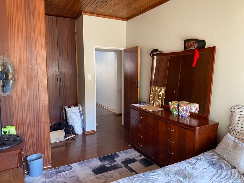 A bedroom featuring built-in wooden cupboards, a wooden ceiling, and laminate flooring, offering a dated but functional living space.