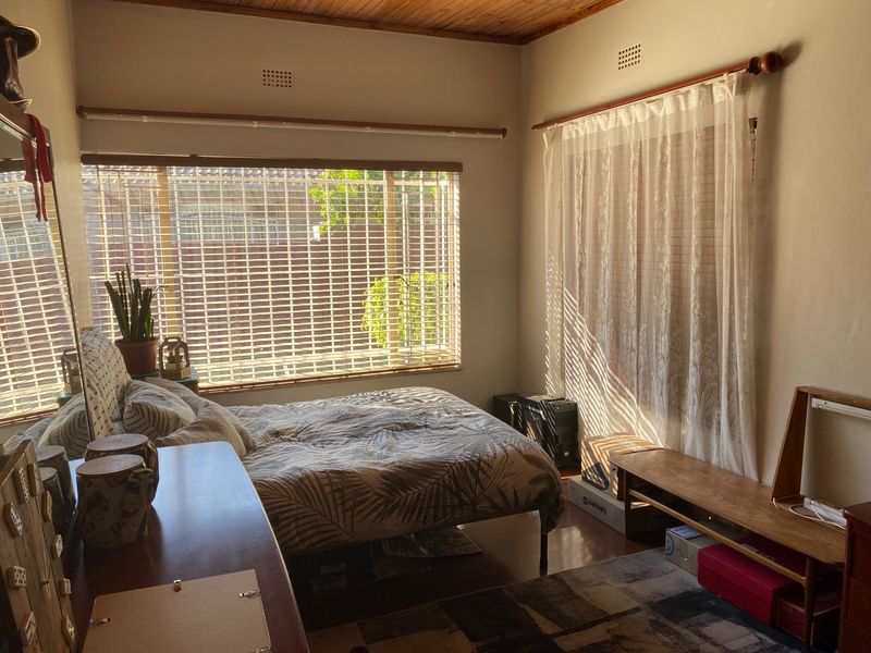 A bedroom featuring timber ceilings, laminate flooring, and large windows with venetian blinds and curtain rods, offering natural light.