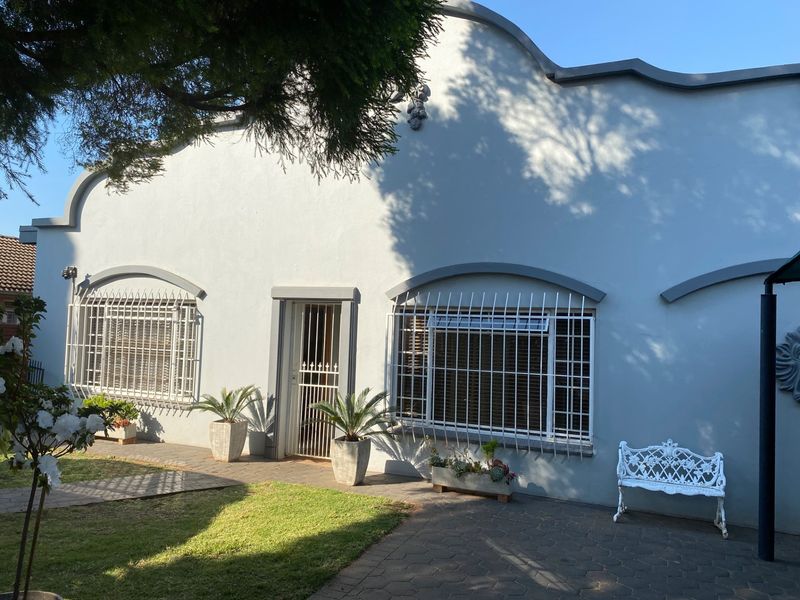 A well-maintained rear exterior view of the apartment featuring a paved patio area, lawn, and secure window bars.