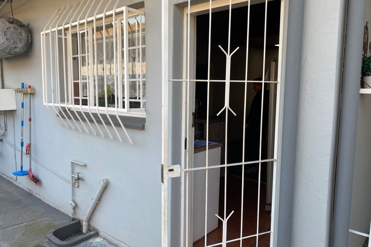 Rear exterior view of the apartment featuring a security gate, window security bars, and external utility plumbing.