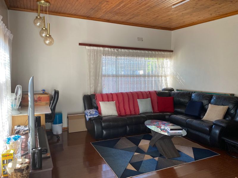 A living room featuring a timber-paneled ceiling, laminate flooring, and pendant lighting, offering a functional space with potential for modern updates.